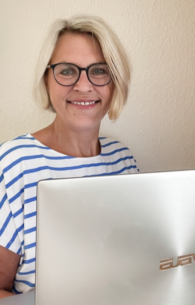 Patricia Wandt - Bürodienstleistungen - steht mit Laptop lächelnd an der Wand
